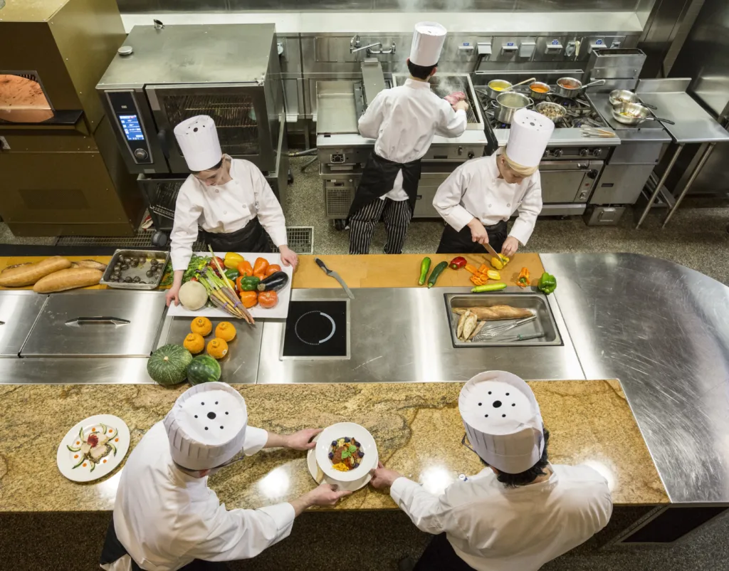 Chefs prepare meals at restaurant kitchen work tables.- A Quick Guide to Commercial Kitchen Work Tables - Chef's Deal 