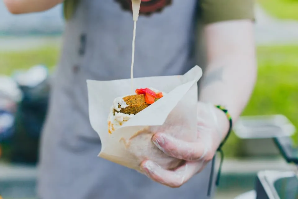 a male chef prepares one of the popular street foods, falafel, pours sauce into it - Chef's Deal