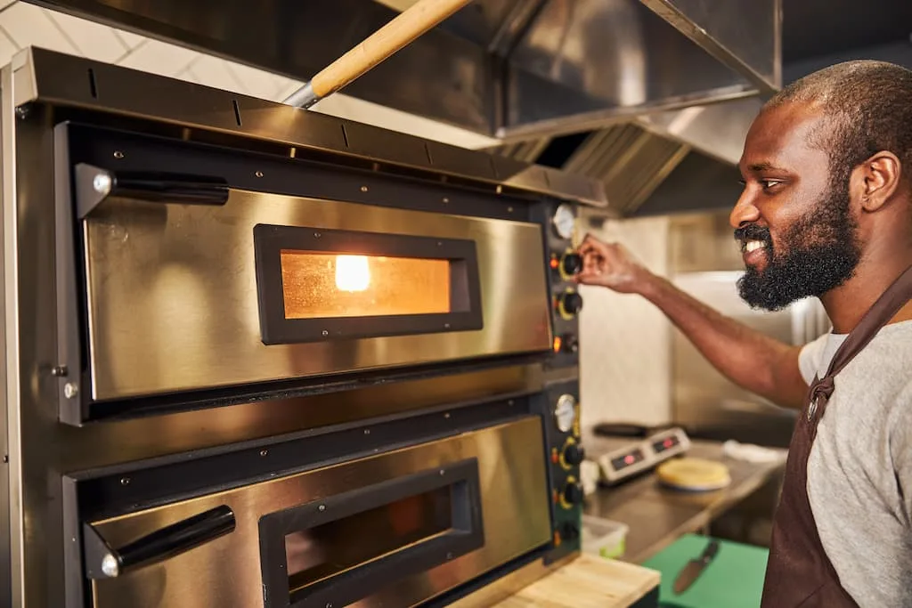 Proper Use and Handling extends your commercial kitchen equipment lifespan. A cook bakes food in an commercial oven in a restaurant kitchen.