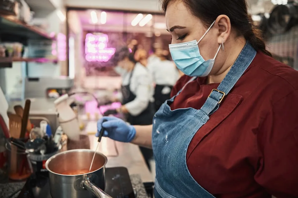 Importance of Food Preparation and Cooking equipment in food safety - Cook is preparing meal her hands in gloves and a mask on her face. 