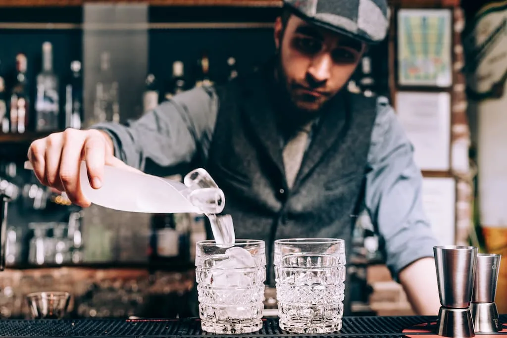 Bbarman is preparing cocktails and pouring ice and wiskey.