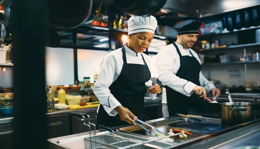 2 chefs are preparing meal at a central cook station of a small commercial kitchen.