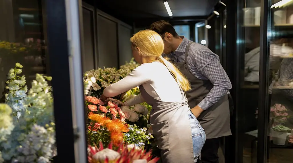 Two florists are arranging fresh flowers in the flower display coolers